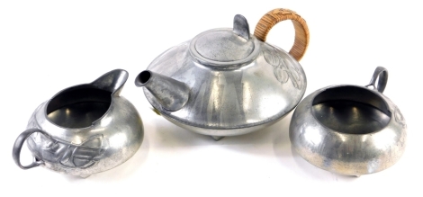 An early 20thC Archibald Knox design English Pewter three piece tea service, comprising teapot of squat circular form, raised with lotus flowers, with T scroll handle, 10cm high, milk jug and sugar bowl marked 0231. (3)