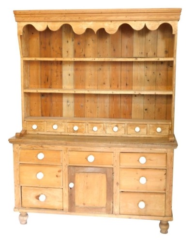 A Victorian stripped pine kitchen dresser, with plate rack top having seven spice drawers with ceramic knob handles, and an arrangement of drawers and cupboards to base, on turned legs, 200cm high, 153cm wide, 49cm deep.