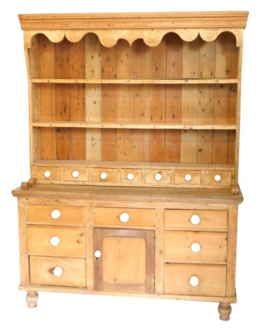 A Victorian stripped pine kitchen dresser, with plate rack top having seven spice drawers with ceramic knob handles, and an arrangement of drawers and cupboards to base, on turned legs, 200cm high, 153cm wide, 49cm deep.