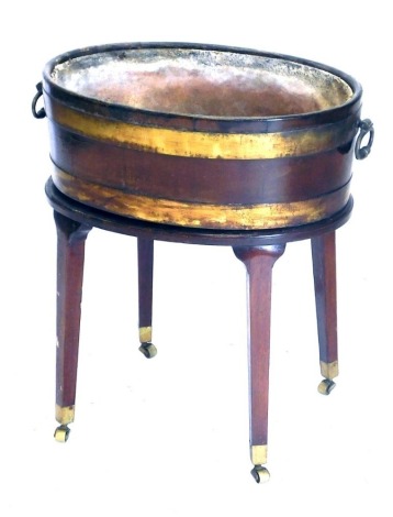 A Regency mahogany wine cooler, with brass banded oval vessel with loop handles and liner, the base on square taper legs, with brass cup castors, 66cm high, 60cm oval over handles.