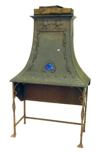 An Arts and Crafts brass fire canopy or chimney canopy, with Ruskin enamelled heart shape jewel, on wrought iron stand for an open fire, 98cm high (exposed), 108cm wide, 50cm deep plus base.