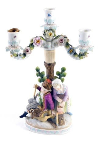 A Dresden porcelain candelabrum, modelled in the form of a young man and lady with sledge, etc., 32cm high. (AF)