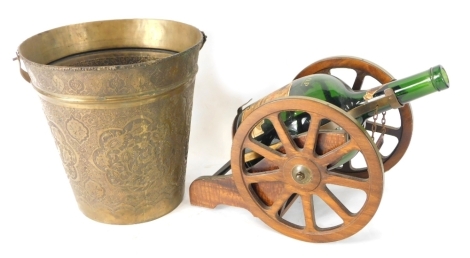 An early 20thC brass bucket, with swing handle, the tapering body elaborately repousse decorated with scrolls and flowers, 26cm high, and a brandy barrel cannon decanter, with vacant bottle of brandy. (2)