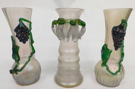 A pair of early 20thC Loetz style ribbed glass vases, each raised with berries and vines, in green on clear ground, unmarked, 24cm high, and a further Loetz style Art Nouveau glass vase. (3)