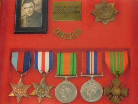 A cased WWII medal group, comprising 39-45 and France and Germany Stars, Campaign and Victory medals, and a cross, with red and green ribbon, Lincoln Regiment badge and photograph, in case marked CAPT D. COOKE Fourth Battalion Lincolnshire Reg W.W.II, the