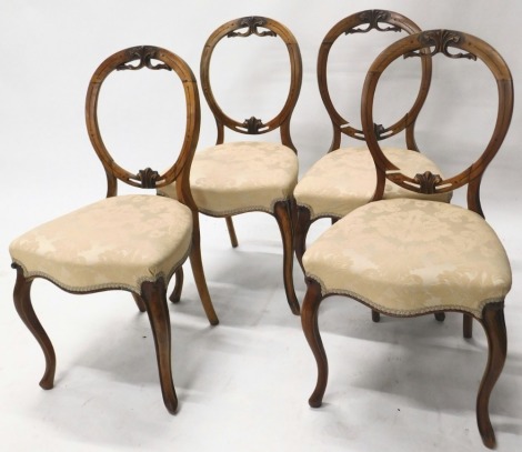 A set of four Victorian walnut balloon back dining chairs, each with a cream upholstered padded seat, on cabriole legs.