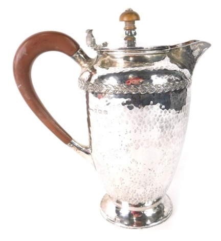 A George V Arts and Crafts silver hot water jug, by A. E. Jones Ltd, with wooden lock and composition handle, the main body with hammered decoration and with a band of laurel, Birmingham 1931, 18cm high, 15.2oz all in. (AF)