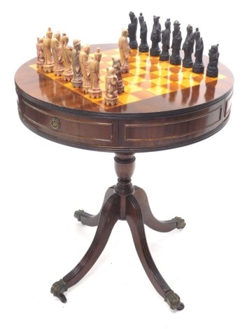 A 20thC mahogany drum games table, with inlaid chequer board top and real and dummy cock beaded drawers, containing various chess pieces, on a turned baluster stem terminating in quadruple sabre legs terminating in lion's paw feet and castors, 70cm high, 