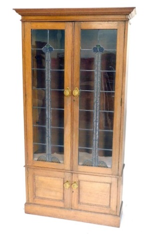 An early 20thC oak Arts and Crafts bookcase, the moulded cornice raised above a pair of lead glass panel doors, with coloured glass orbs and frosted and textured glass sections, with Aesthetic brass handles, above a double cupboard on block base, 192cm h