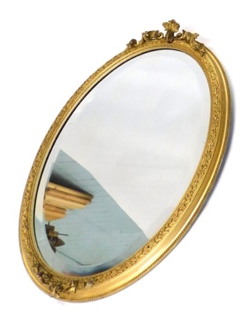 A 20thC gilt wood oval hanging mirror, the bevelled glass surmounted by scroll carving in a heavily carved floral and bead frame, 71cm high 53cm wide 6cm deep.