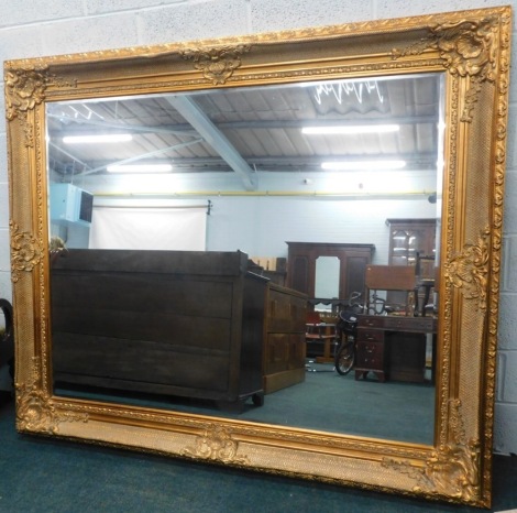 A very large giltwood rococo style hanging mirror, the bevel glass, the moulded frame decorated with scrolls and flower heads, 191cm high, 163cm wide, 9cm deep.