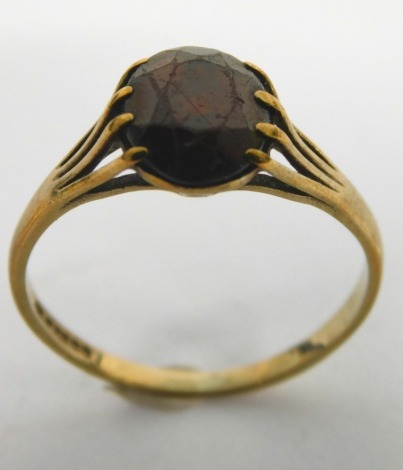 A 9ct gold dress ring, claw set with red stone, on a textured part pierced shank, 1.5g all in.