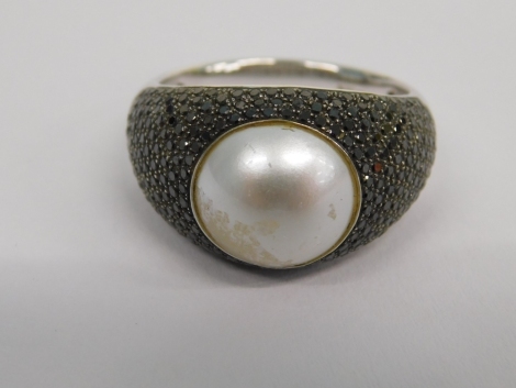 A 18ct white gold blister pearl and black diamond dress ring, the central pearl in a rub over setting with pave set black diamond shoulders, 7.8g all in.