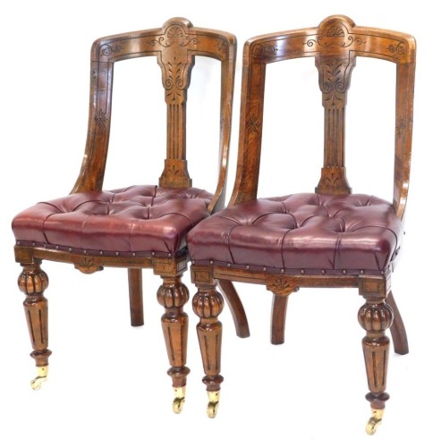 A pair of Victorian oak dining chairs, each with heavily carved vertical splats, over stuffed seats in red studded leather, shaped fronts and turned reeded front legs, 91cm high. (2)