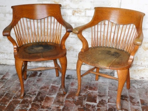 A pair of Edwardian oak office chairs, with spindle backs and saddle seats.