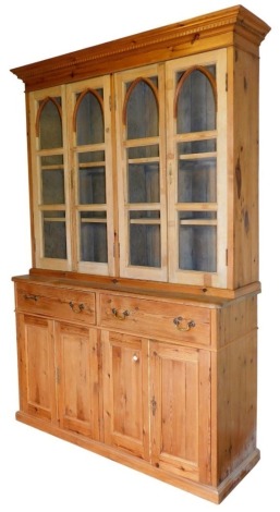 A Victorian stripped pine bookcase dresser, with dentil moulded cornice, Gothic arch glazed four door top, over two drawers and two panelled doors, on a plinth base, 228cm high, 148cm wide, 48cm deep.