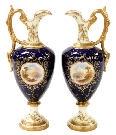 A pair of Coalport porcelain ewers, each decorated with a reserve depicting Loch Katrine and Loch Garry, against a cobalt blue ground with gilt highlights, gilt leaf moulded handles, circular face, stamped to underside and numbered 7586/3/5149, and retail