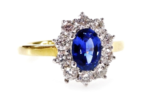 An 18ct gold sapphire and diamond cluster ring, with central oval cut sapphire in a platinum four claw setting, 6.8mm x 5.2mm x 2.8mm, approximately 0.68ct, surrounded by ten round brilliant cut diamonds, each approximately 0.10ct, in a raised basket on a