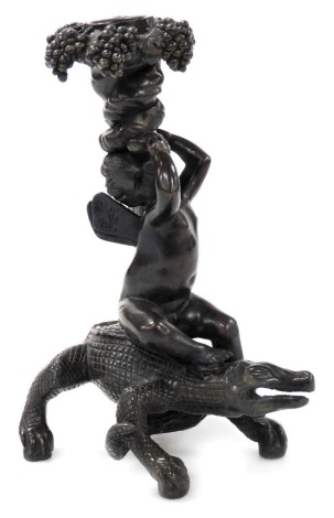 An early 20thC bronze Bacchanalian figural candlestick, in the form of a Bacchanalian cherub seated on a crocodile supporting a fruiting vine sconce, 19cm high.