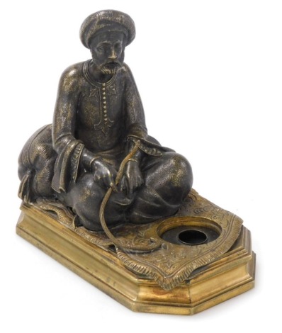 A 19thC bronze patinated figure of a Middle Eastern gentleman, seated on a carpet, incorporating a small ink receiver and mounted on a formal octagonal brass plinth, 14cm high.