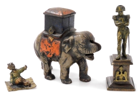 A small 19thC bronze statue of Napoleon, in a standing pose with folded arms, on a square plinth, together with a small cast bronze patinated and painted figure of an Oriental child on a rug, and a cast iron model of an elephant, trunk lacking. (3)