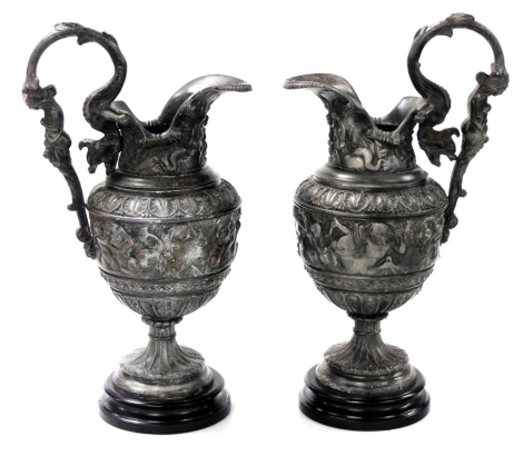 A pair of late 19thC white metal Cellini ewers, in the Renaissance style, with figural handles and lappet borders above a band of classical figures, raised on turned ebonised socles, 44cm high.