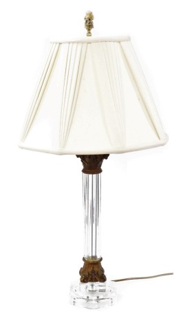 A glass column table lamp, with gilt metal Corinthian capital and octagonal base, with pleated silk shade and simulated ivory Oriental figure, 85cm high.