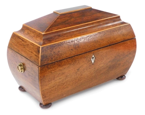 A Regency rosewood and boxwood strung sarcophagus shaped tea caddy, the hinged lid enclosing fitted interior with two lidded caddies and a mixing bowl, the base with brass ring handles, on bun feet, 32cm wide.