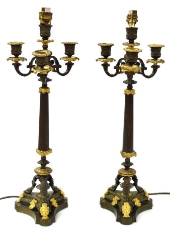 A pair of bronzed and gilt metal table lamps, in Empire style, each with a reeded column, four candle arms, on a triform base decorated with dolphins, etc., converted at a later date, 60cm high. (AF)