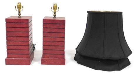 A pair of Chinese simulated red lacquer square section table lamps with shades, the lamp bases measuring 34cm high, with black shades.