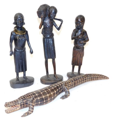 Three African tribal figures, comprising a man carrying produce on his shoulder, 41cm high, and two women, 35cm and 38cm high, together with a wooden carving of a crocodile, 47cm wide. (4)