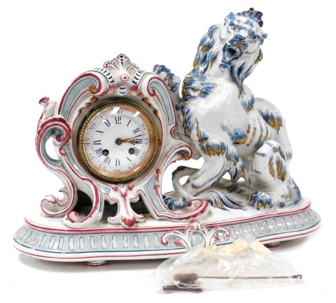 A late 19thC Sarreguemines faience cased mantel clock, circular enamel dial bearing Roman and Arabic numerals, eight day movement by Japy Freres et Cie with bell strike, the case of scrolling rococo form, flanked to the right by a rampant lion, raised on 