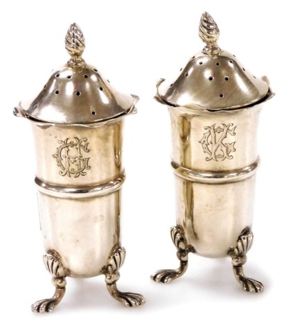 A pair of late Victorian silver pepperettes, each with a flame finial, waved rim and cylindrical body with raised central band, monogram engraved, on three paw feet, William Davenport, Birmingham 1900, 2.61oz, 9cm high.