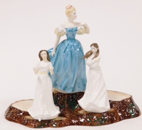 Three Royal Doulton porcelain figures, modelled as Enchantment, HN2178, Embrace, HN4258, and Sentiments Greetings, HN4250, together with a Beswick pottery display stand, modelled as tree stumps, 30cm wide.