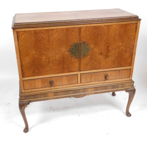 A mid century walnut drinks cabinet, with a pair of doors opening to reveal a single shelf, above two frieze drawers, raised on shell capped cabriole legs, 108cm high, 108cm wide, 41cm deep.