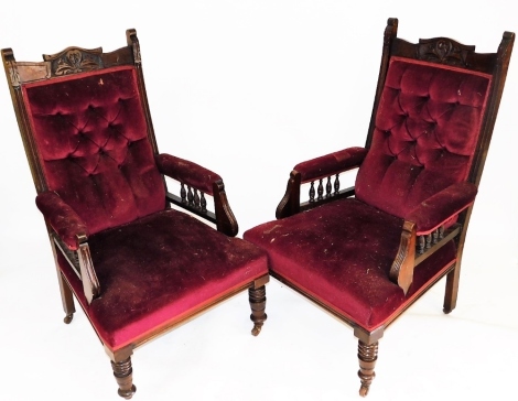 A pair of Victorian mahogany armchairs, upholstered in claret button back draylon and overstuffed seats, raised on turned legs, capped on castors, 66cm wide.