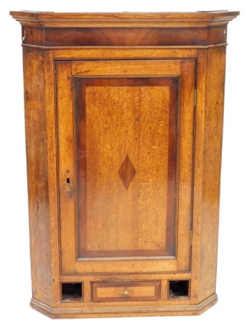 A George III oak and mahogany hanging corner cupboard, the top with a moulded edge above a panelled door, set with a mahogany diamond panel, above three drawers (two missing), 114cm high, 76cm wide.