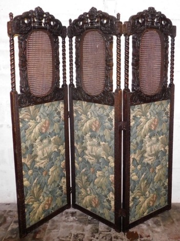 An early 20thC carved oak three fold screen in Carolean style, each part carved with putti, flowers, scrolls, etc., surrounding a caned insert above a tapestry effect panel, 182cm high, 180cm wide.