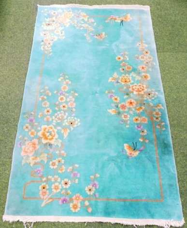 A Chinese wool rug, decorated with flowers, on a jade green ground, possibly 1920s, 118cm x 207cm.