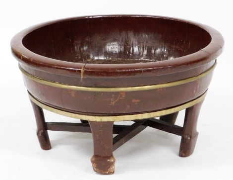 A 19thC Chinese circular wooden wash basin, with brass coopered bands, on shaped legs with X shaped stretcher, 36cm high, 69cm diameter.