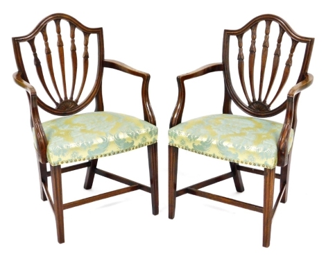 A pair of Hepplewhite style mahogany elbow chairs, possibly early 20thC, each with a shield shaped back, shaped arms, and gold and blue damask upholstered padded seat, on channelled legs with H stretcher.