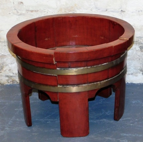 A Chinese red painted wooden wash basin, with brass coopered bands, on plain supports, 39cm high, 53cm wide.