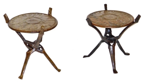 A near pair of African folding occasional tables, the circular tops carved with a rhinoceros, elephant, and hippopotamus, raised on three figural folding legs, 42cm high, 41cm wide.