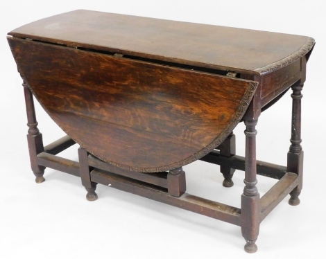 An 18thC oak drop leaf gate leg dining table, the top with a carved border, raised on turned legs, united by a box stretcher, 70cm high, 122cm wide, 46cm wide, 132cm extended.