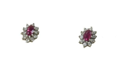 A pair of 9ct white gold ruby and diamond earrings, each formed as a cluster with central oval cut ruby surrounded by ten round brilliant cut tiny diamonds, each in a white claw setting, on single pin back with matched different backs, 2g all in, boxed.