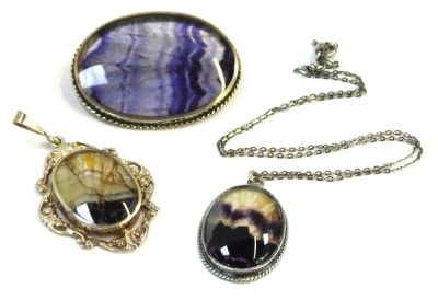 Three Blue John and Blue John style pendants, comprising one with a scroll borders, 3cm x 2.5cm, one in silver frame with a chain marked 925, and another formed as a brooch, with white metal border, unhallmarked but bearing initials H/M 4cm x 3cm. (3)