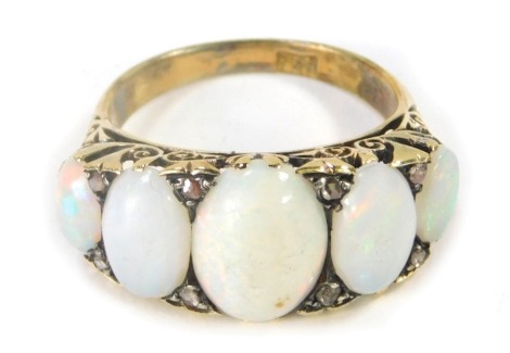 A Victorian opal and diamond dress ring, set with three oval opals, with eight tiny diamond set breaks, the central opal 11mm x 6.8mm x 3.4mm, with scroll design sides, yellow metal stamped 18ct, ring size R½, 6.4g all in.