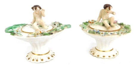 Two late 19thC porcelain small urns and covers, each with a putto finial, and a flower encrusted border picked out in gilt, one with two handles, 8cm high. (AF overall).