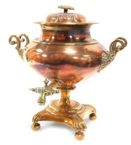 A Regency brass and copper twin handled tea urn, and cover with a floral finial, with brass tap, raised on a foliate capped brass base, on bun feet, 41cm high.