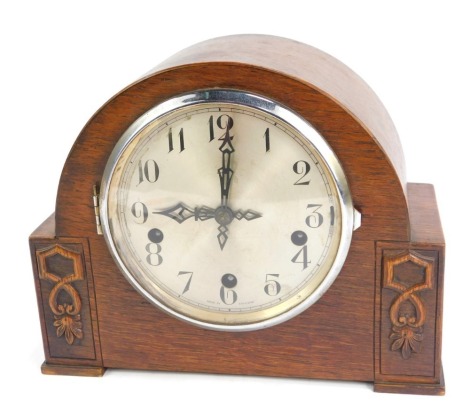 A 1950s Enfield oak cased mantel clock, with a silvered numeric dial, eight day movement with Westminster chimes, the domed case with carved floral supports, with key, 21cm high, 27cm wide, 12cm deep.